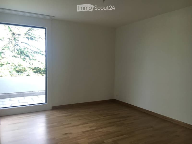 Empty room with wooden flooring, large window, and white walls.