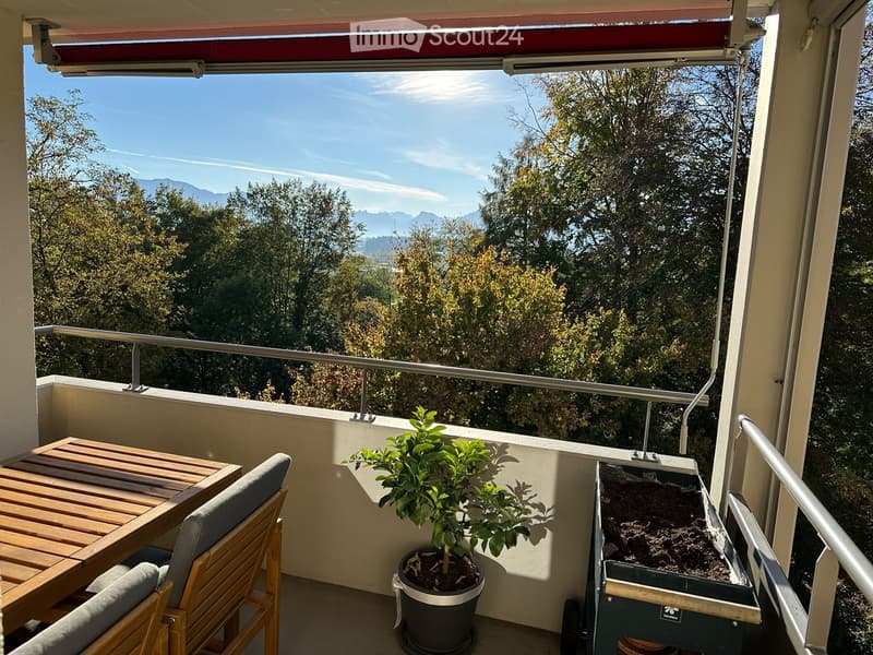 Balcony with wooden table, chairs, potted plant, and scenic mountain view.