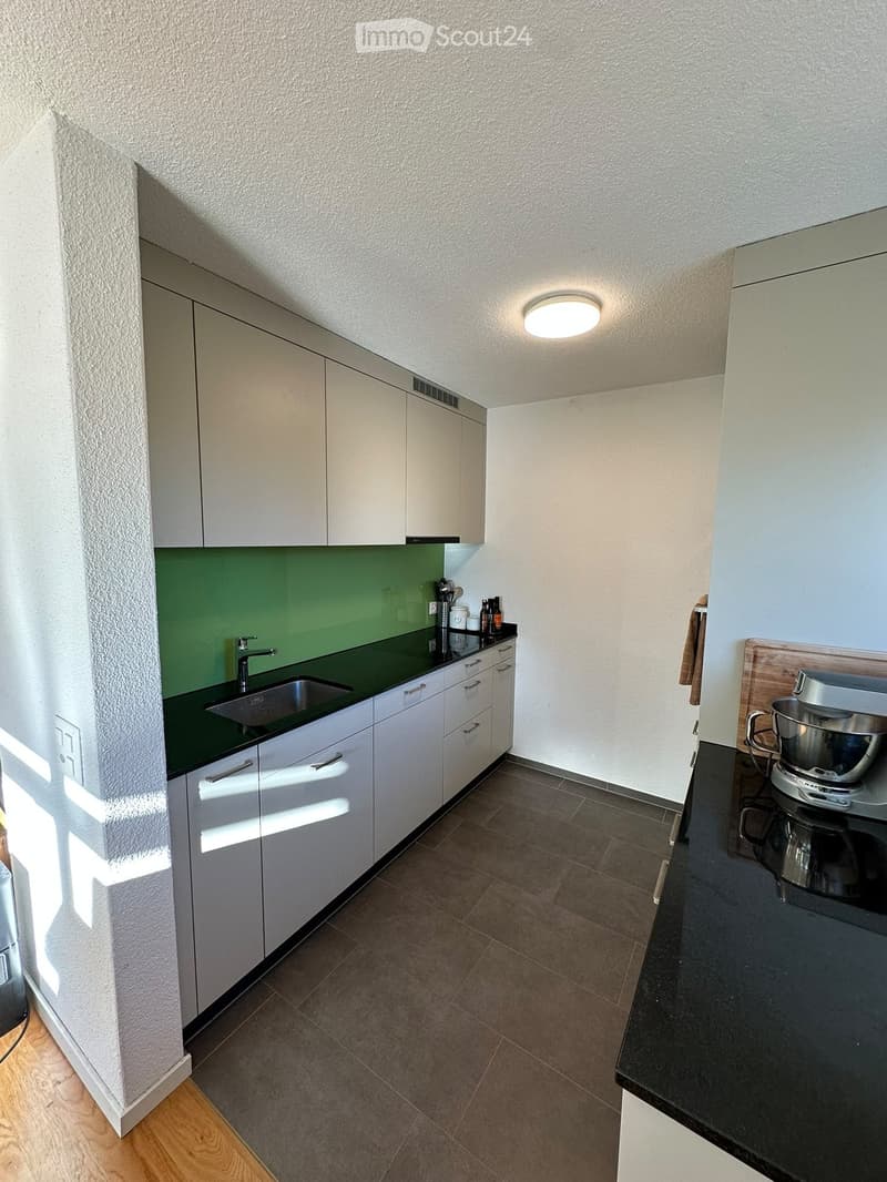 Modern kitchen with white cabinets, green backsplash, dark countertops, and a mixer on the counter.