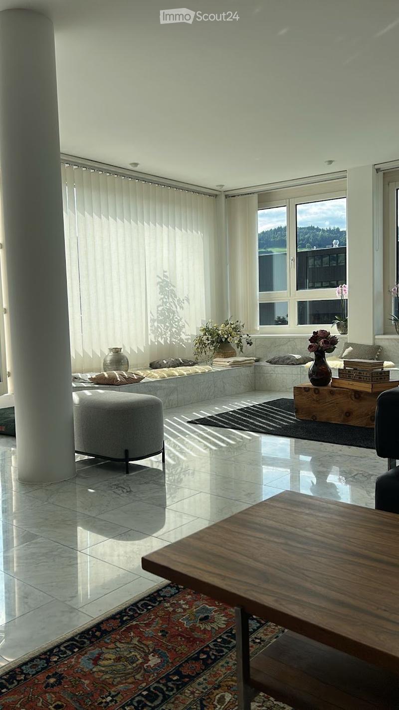 Bright living room with large windows, white walls, polished tile floor, and a mix of modern and traditional furniture including a sofa, coffee table, ottoman, and decorative vases.