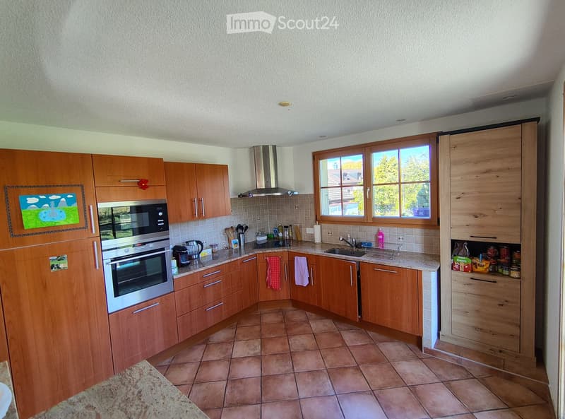Modern kitchen with wooden cabinets, stainless steel appliances, and tiled flooring. Features an oven, microwave, sink, and various kitchen utensils.