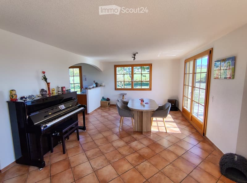 A well-lit room with tiled flooring, a grand piano, a small round table with chairs, and decorative items on a shelf.