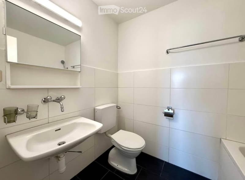 Modern bathroom with white tiles, a sink, toilet, mirror, and towel rack.