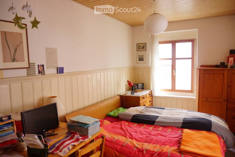 Cozy bedroom with a bed, a chair, a table, a lamp, a screen, a radiator, a cupboard, and a picture on the wall.