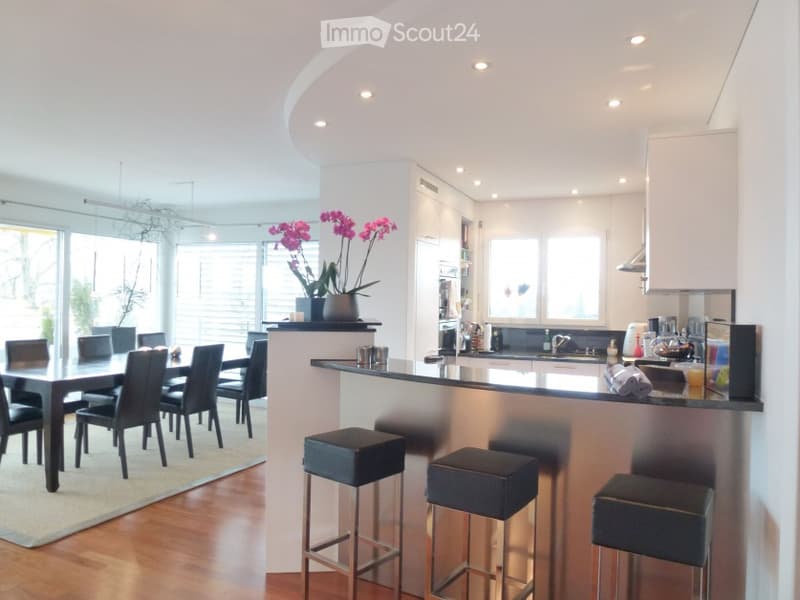 Modern open-plan kitchen and dining area with a sleek black dining table and chairs, a kitchen island with bar stools, and contemporary kitchen cabinets and appliances.