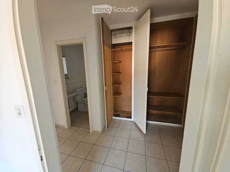 Empty hallway with tiled floor, open closet with wooden shelves, and access to a small bathroom with a toilet and sink.