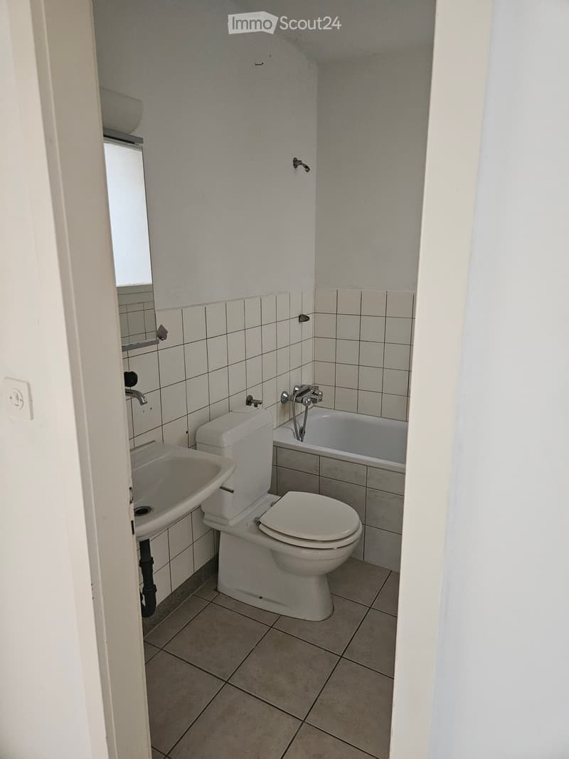 Small bathroom with white tiled walls, a toilet, a sink, and a bathtub.