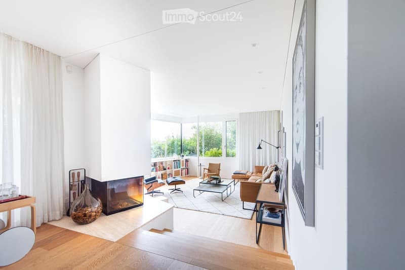 Bright living room with large windows, fireplace, sofa, coffee table, chairs, bookshelf, and floor lamp.