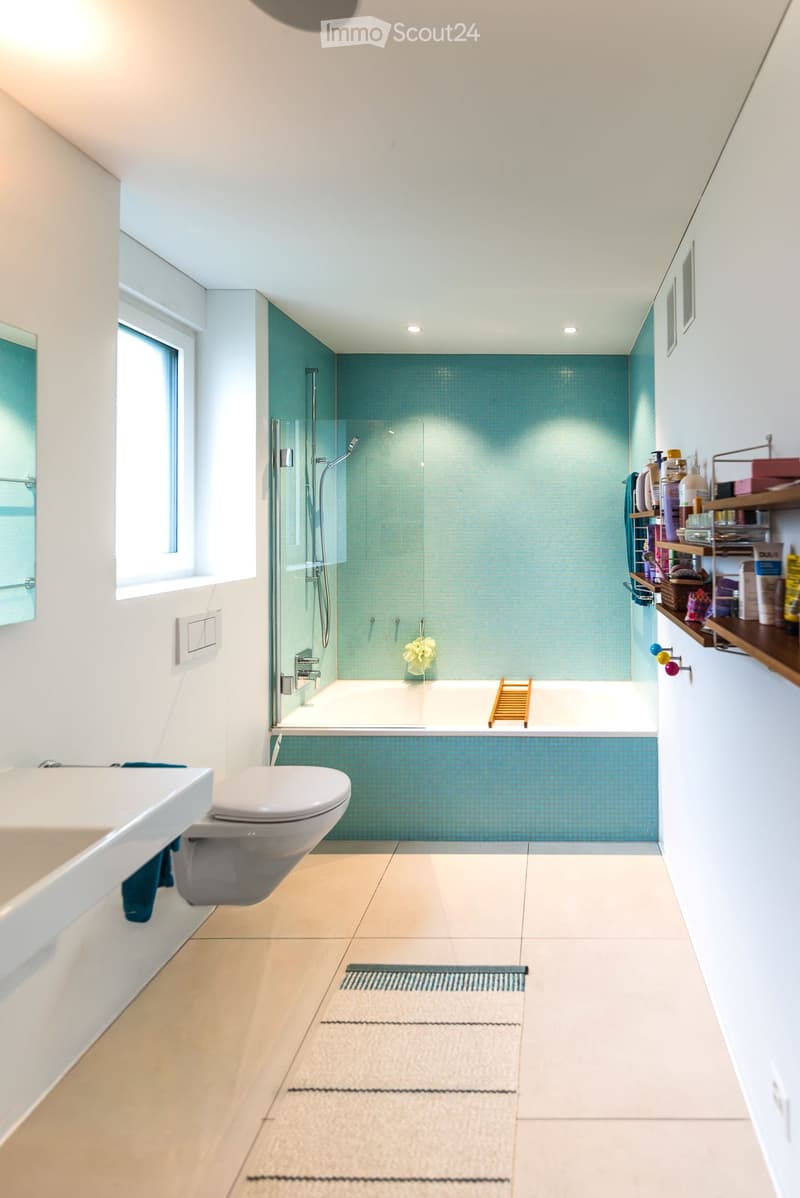 Modern bathroom with a bathtub, toilet, glass-enclosed shower, and wooden shelf with toiletries.