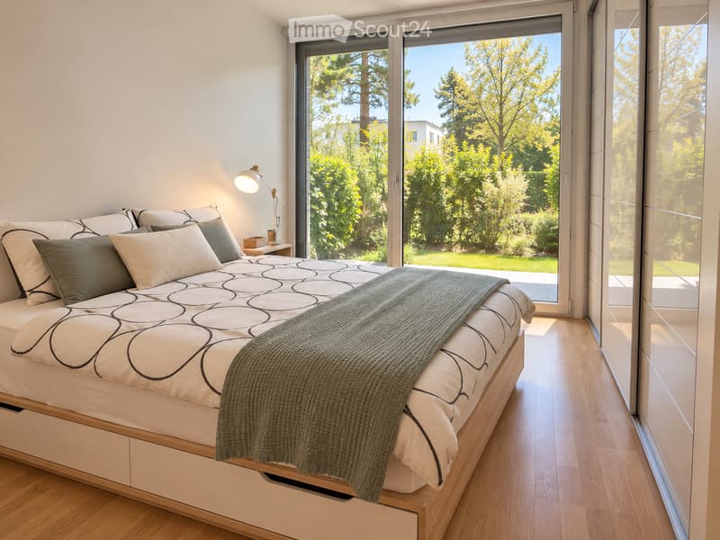 Modern bedroom with a large bed, patterned bedding, pillows, a nightstand, and a wall-mounted lamp. Large windows offer a view of greenery outside.