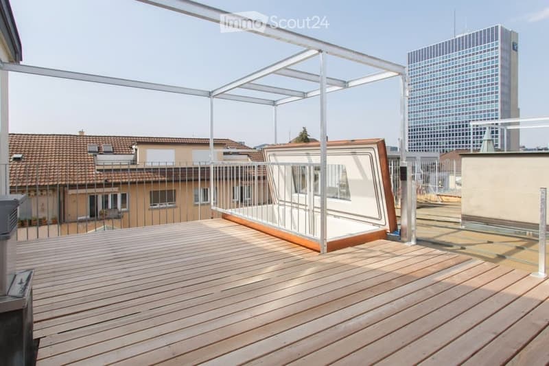 Wooden deck terrace with glass railing, modern design, cityscape view in the background.