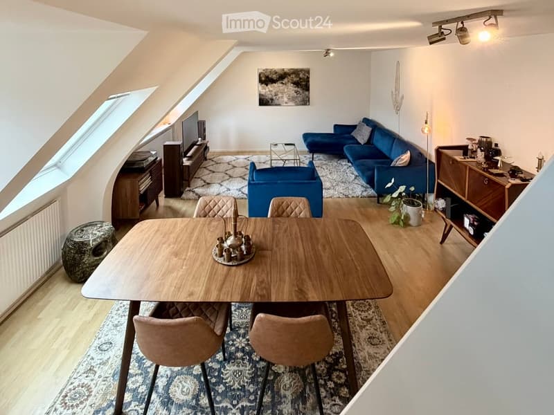 A modern, well-lit living and dining area with a blue sofa, wooden dining table, chairs, television, and decorative items.
