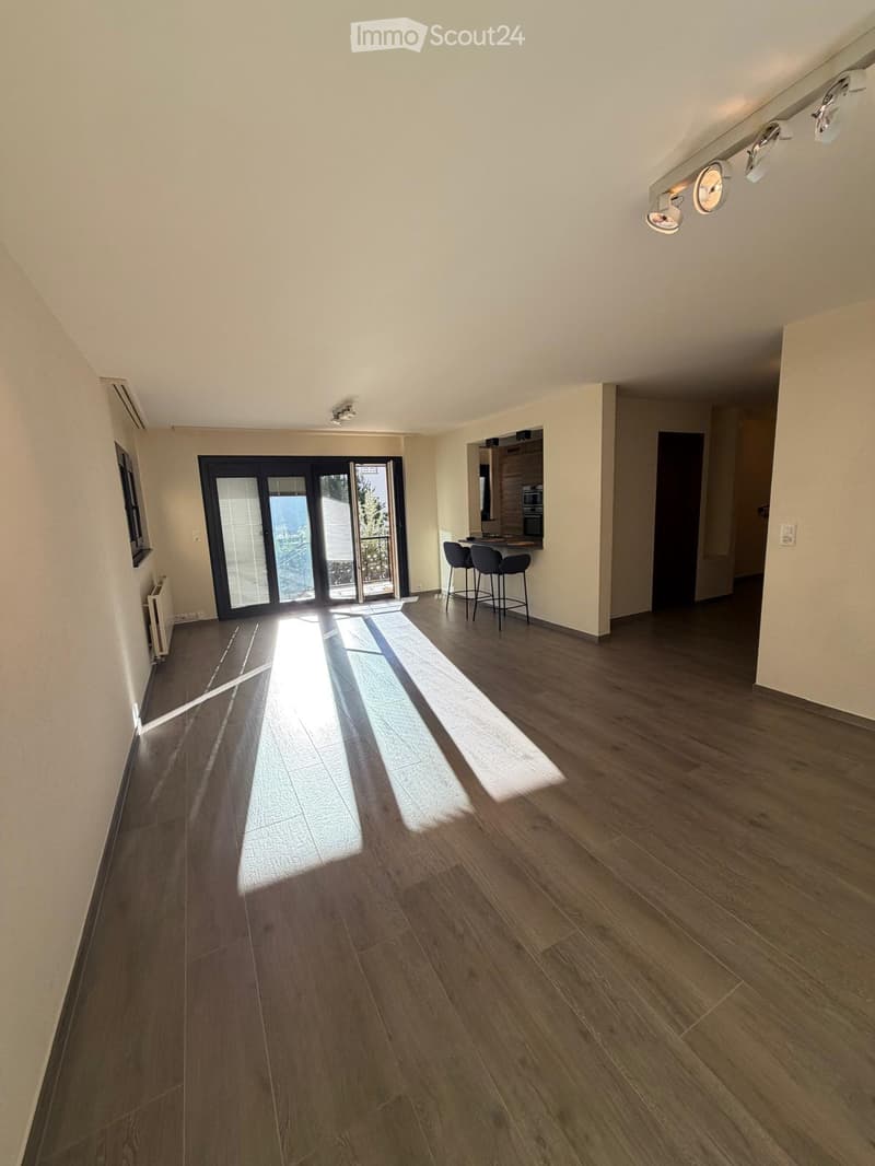 Empty room with wooden flooring, large sliding glass doors leading to a balcony, and natural light streaming in.