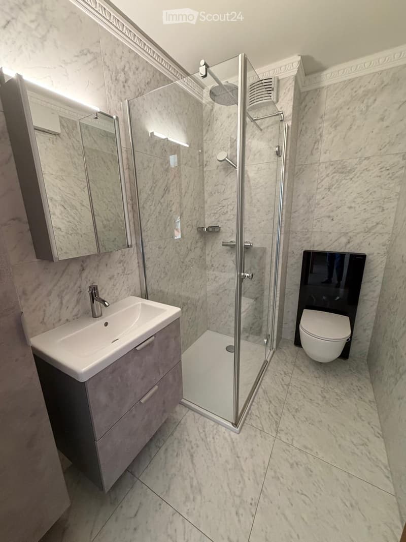 Modern bathroom with marble tiles, a glass-enclosed shower, a sink with a modern faucet, and a toilet.