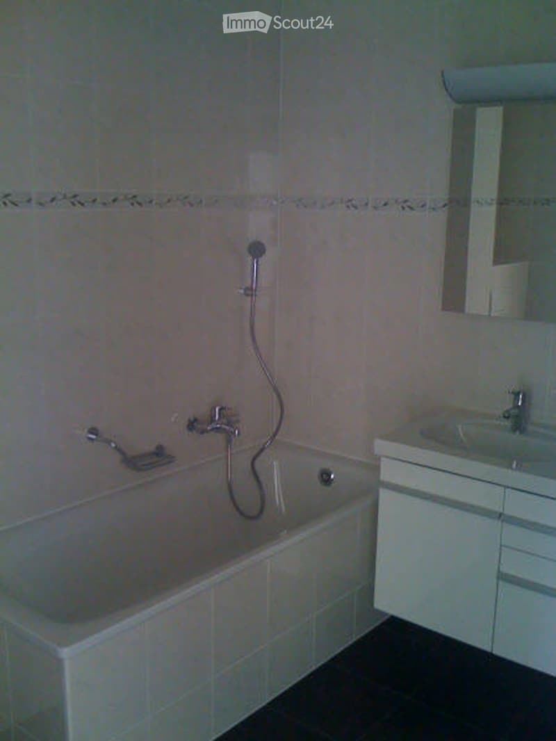 Modern bathroom with a bathtub, shower hose, sink, and cabinet.