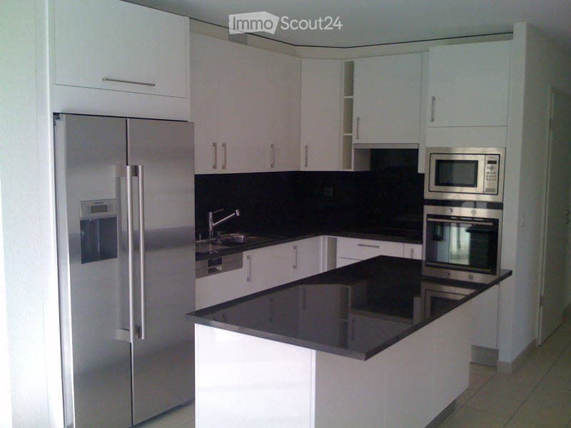 Modern kitchen with white cabinets, black countertops, stainless steel appliances including a refrigerator, microwave, and oven, and a central island.