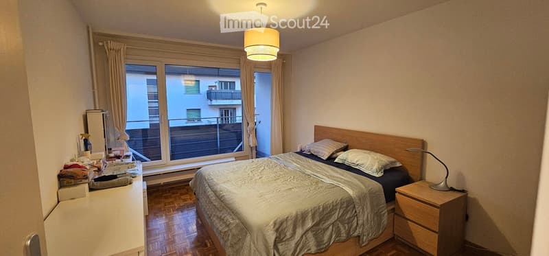 Cozy bedroom with a double bed, nightstand, lamp, and a large window with a view of the city.