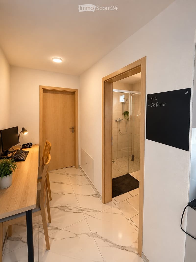 A modern hallway with marble flooring, a wooden desk with a computer, a chair, and a glass-enclosed shower area visible through an open door.