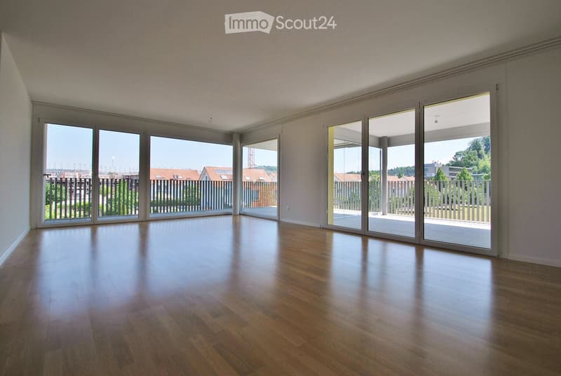 Empty room with wooden flooring and large sliding glass doors leading to a balcony or outdoor area. The walls are painted in a light color, and the space is well-lit with natural light.