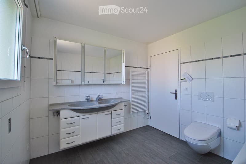 Modern bathroom with white tiles, a double sink, large mirror, white cabinetry, and a toilet.