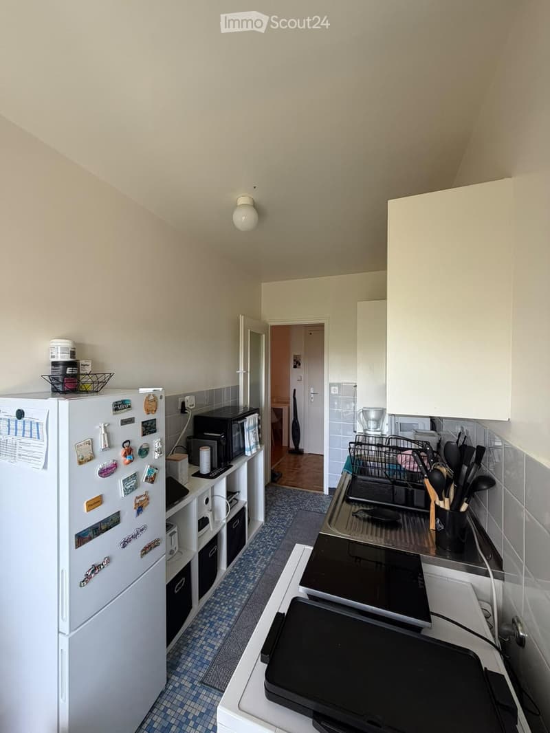 A compact kitchen with a refrigerator, microwave, induction cooktop, and various kitchen utensils. The space features tiled walls and a small open doorway leading to another room.
