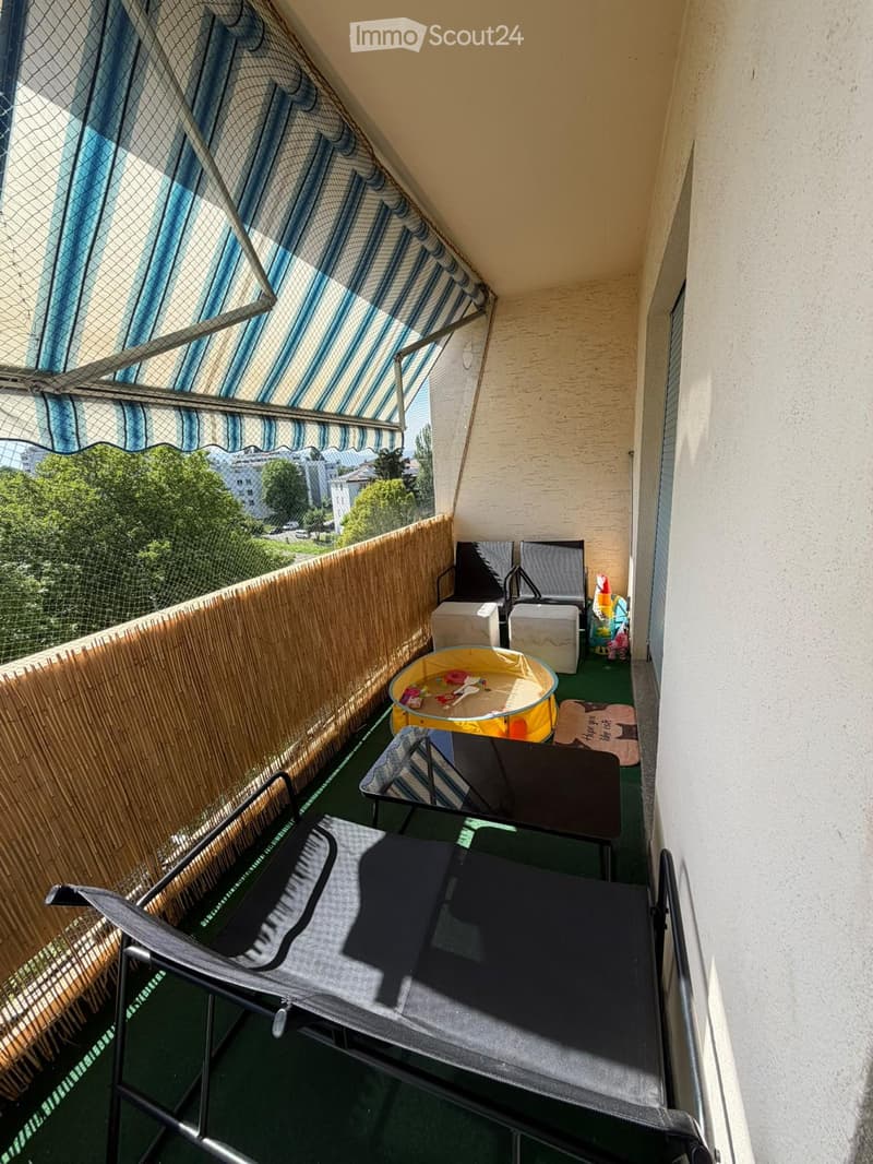 Balcony with a green floor, featuring a lounge chair, a small table, a stool, and a toy play area.