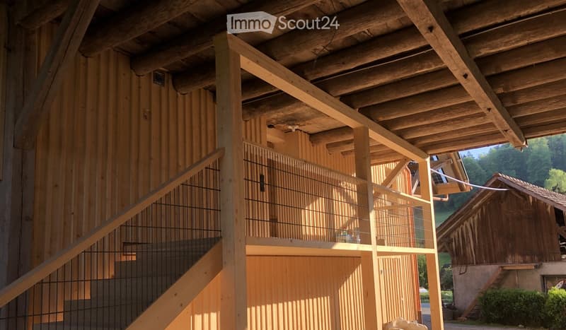 Wooden building with exposed beams, staircase, and balcony overlooking a rural landscape.