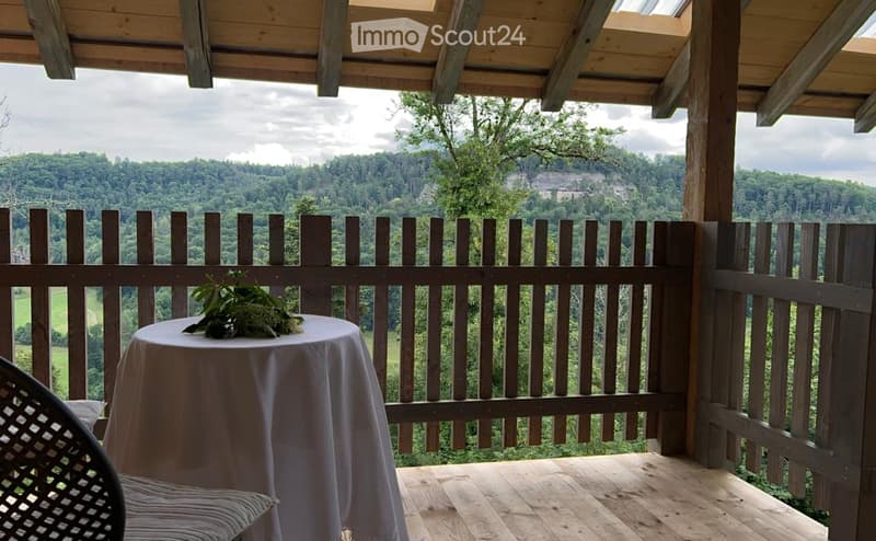 Wooden balcony with a table, chair, and scenic mountain view.