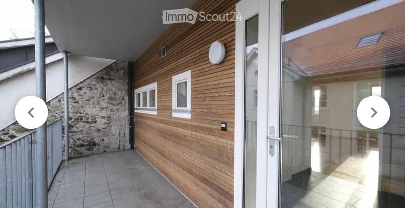Balcony with wooden paneling, tiled floor, glass door leading inside, and a stone wall on one side.