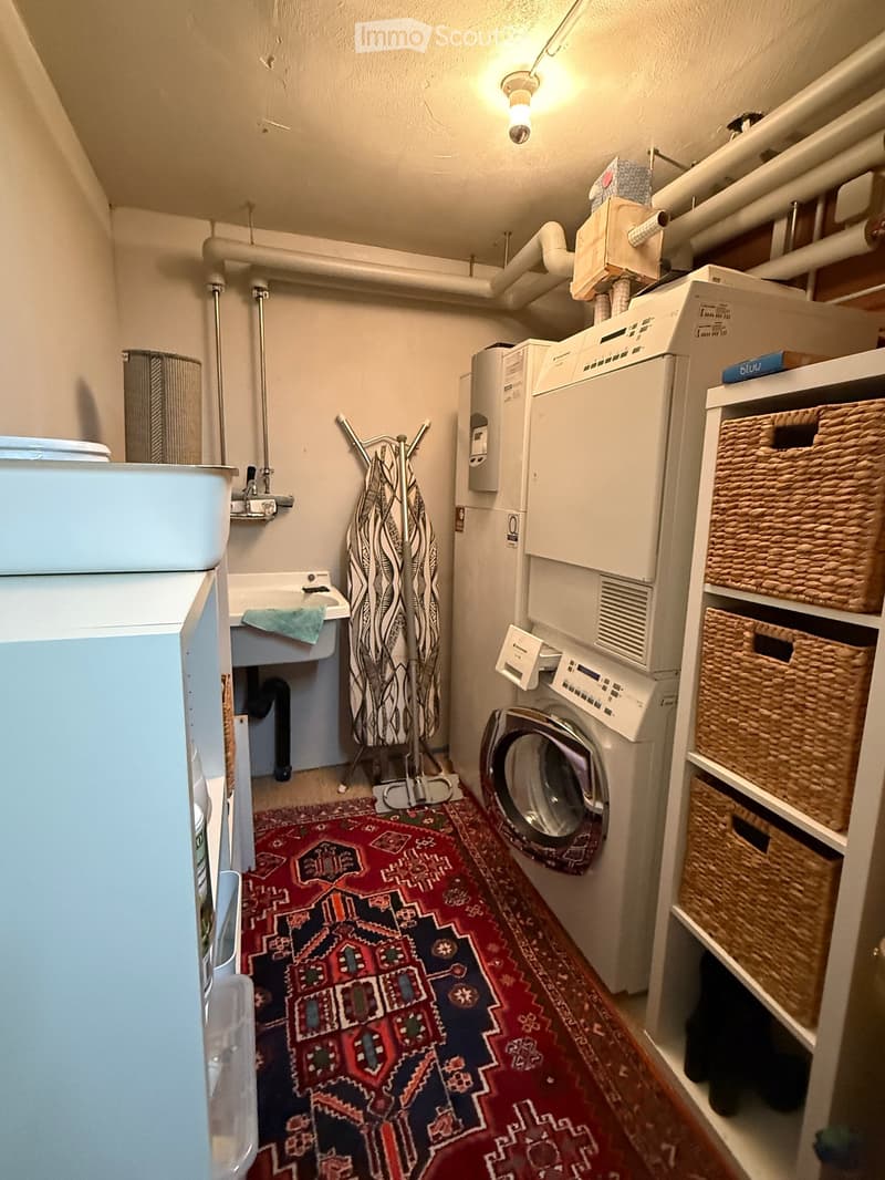 Laundry area with a washing machine, dryer, sink, bathtub, and wicker baskets on a shelf.