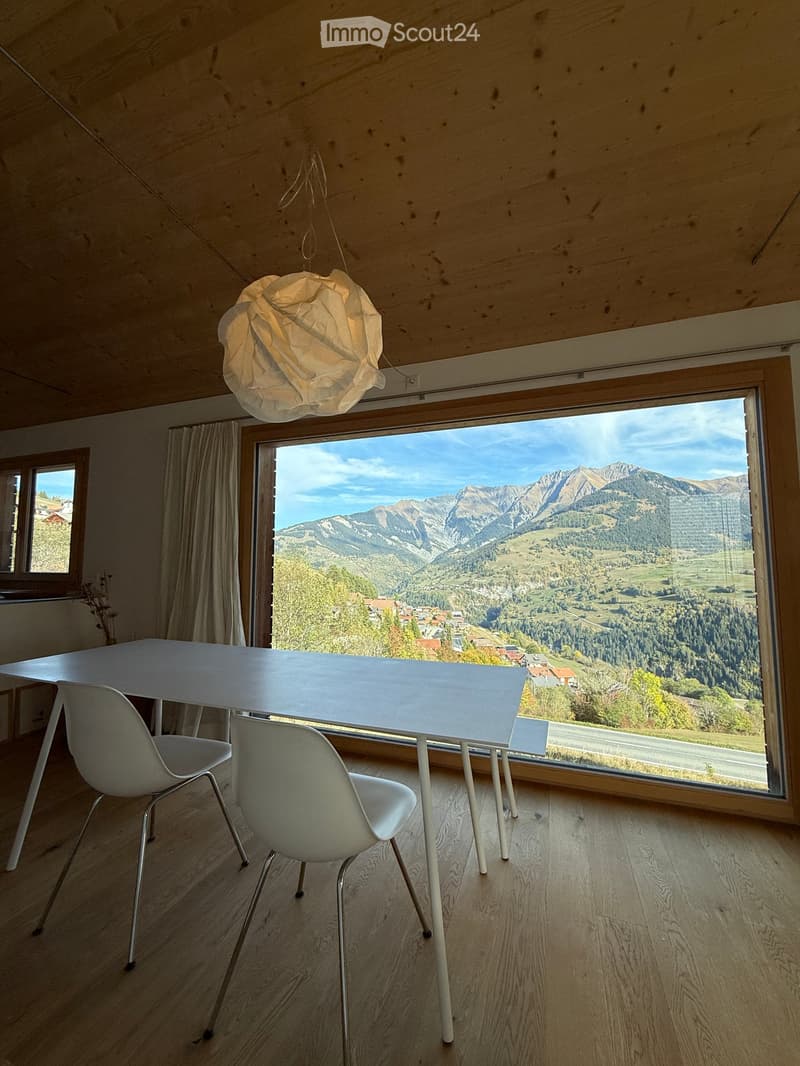 Bright dining area with a white table and chairs, large window offering a scenic mountain view.