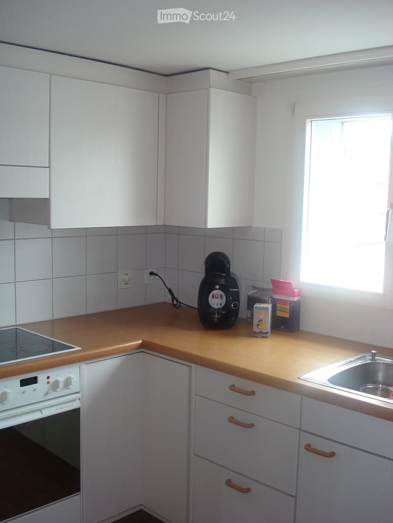 Modern kitchen with white cabinets, wooden countertops, and stainless steel sink. Features an oven, stove, and coffee maker on the counter.