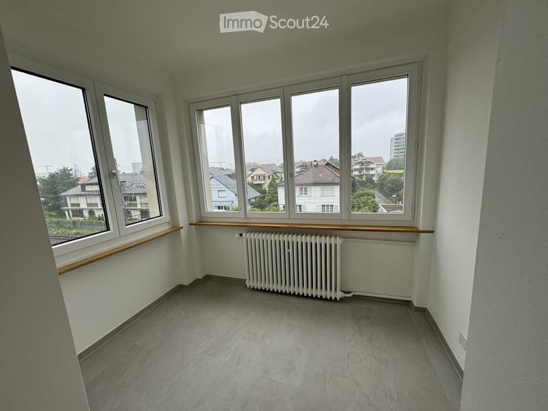 Empty room with tiled floor, white walls, large windows with wooden sills, and a radiator under the windows.