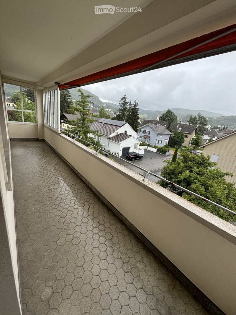 Balcony with hexagonal stone tiles, metal railing, and a view of a residential neighborhood with houses, trees, and a parked car.