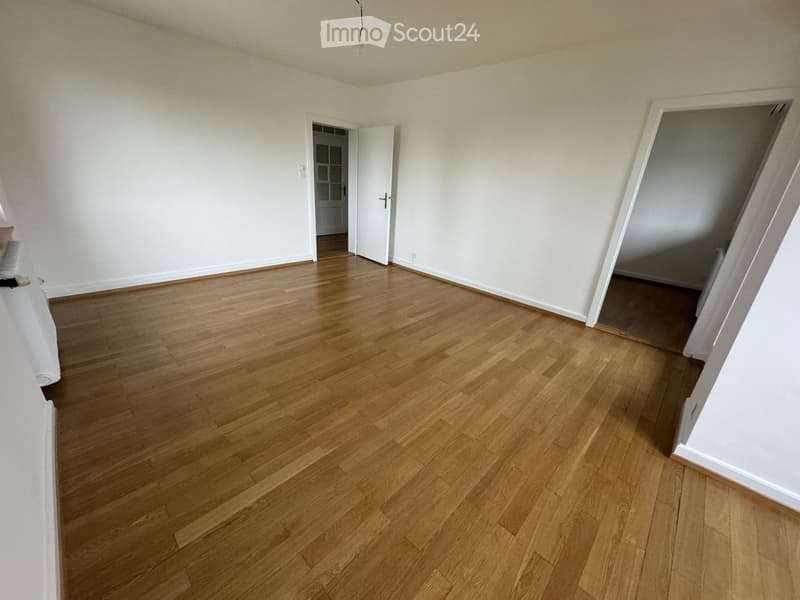Empty room with wooden flooring and white walls, featuring two open doorways leading to adjacent spaces.