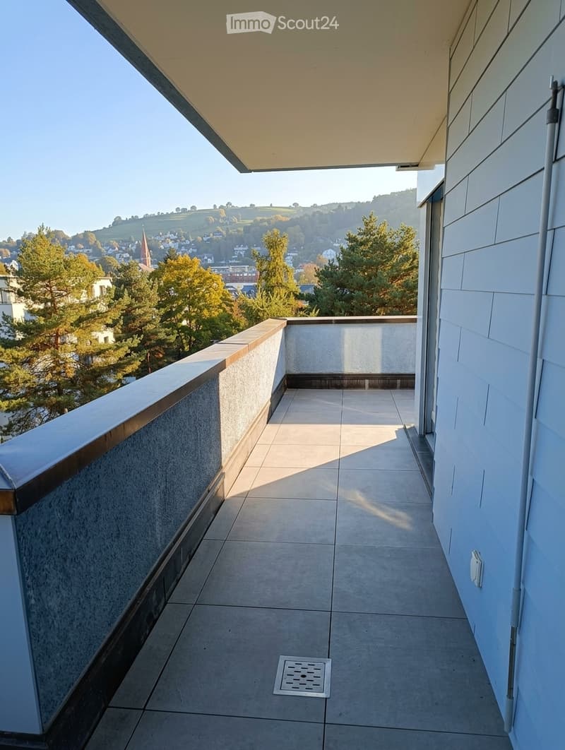 Balcony with tiled floor, modern railing, and scenic view of a town and surrounding landscape.
