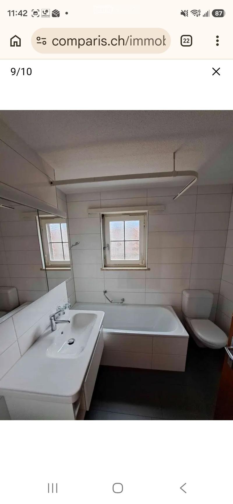 Bathroom with white tiles, a sink, bathtub, toilet, and a mirror. Two windows provide natural light.