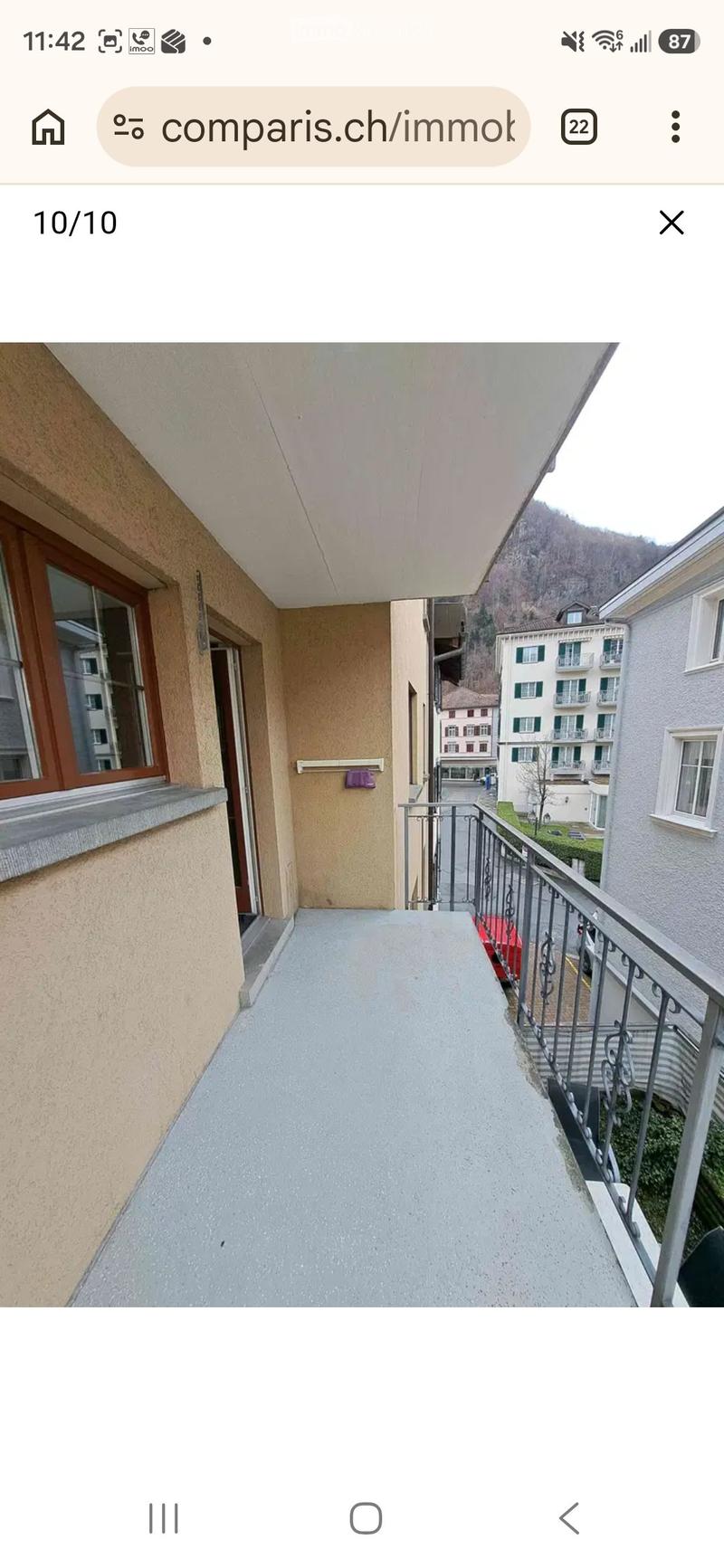 Balcony with metal railing, concrete floor, and view of neighboring buildings and greenery.