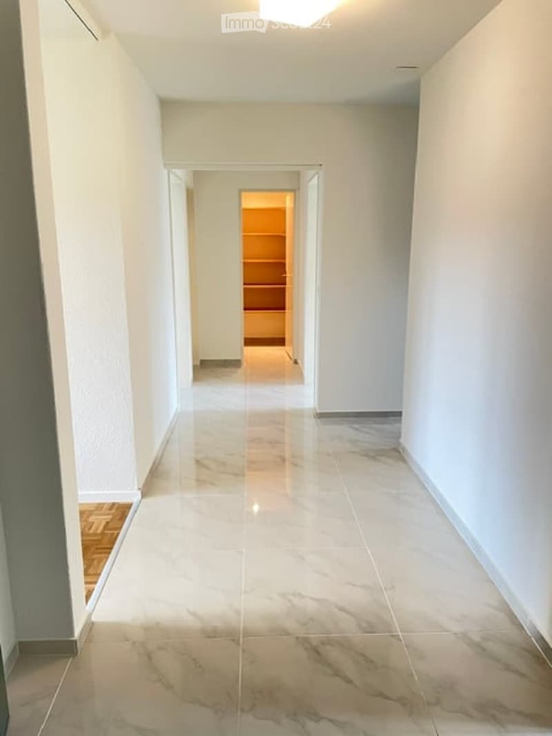 Clean, well-lit hallway with white walls and marble flooring, leading to an open doorway.