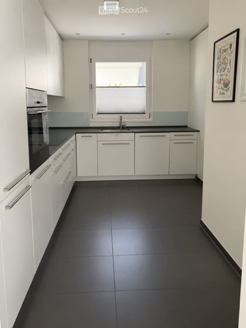 Modern kitchen with white cabinets, black countertops, and black tiled floor. Features a window with blinds, a sink with a faucet, and an oven.