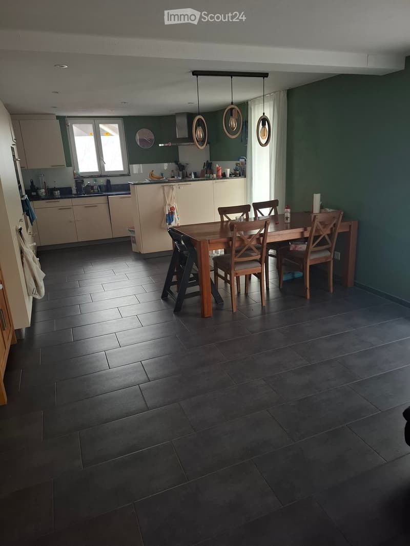 Modern kitchen with dark tiled flooring, light-colored cabinets, and a central dining table with chairs. The kitchen features a sink, refrigerator, and various appliances.