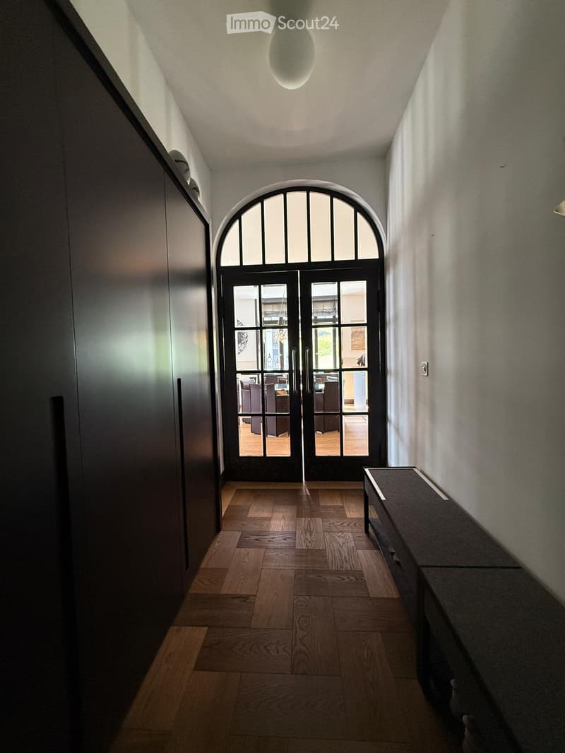 A modern hallway with wooden flooring, a large arched entryway, and a bench on the right side.