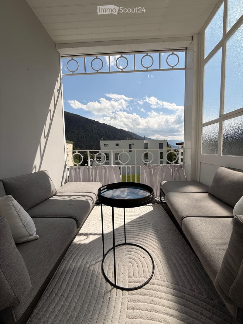 Balcony with a view of mountains, featuring two grey sofas and a round black table.