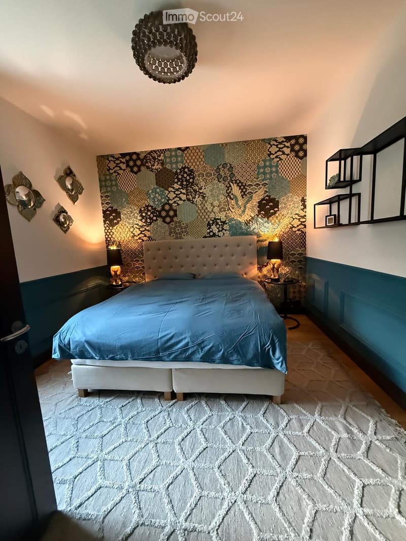 Modern bedroom with a tufted headboard, blue bedding, white shaggy rug, geometric patterned wall art, and decorative mirrors.