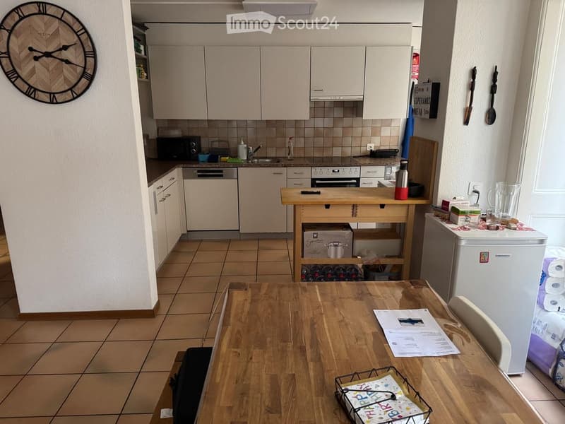 A modern kitchen and dining area with light-colored cabinets, a wooden dining table, and various appliances including a refrigerator, oven, and dishwasher.