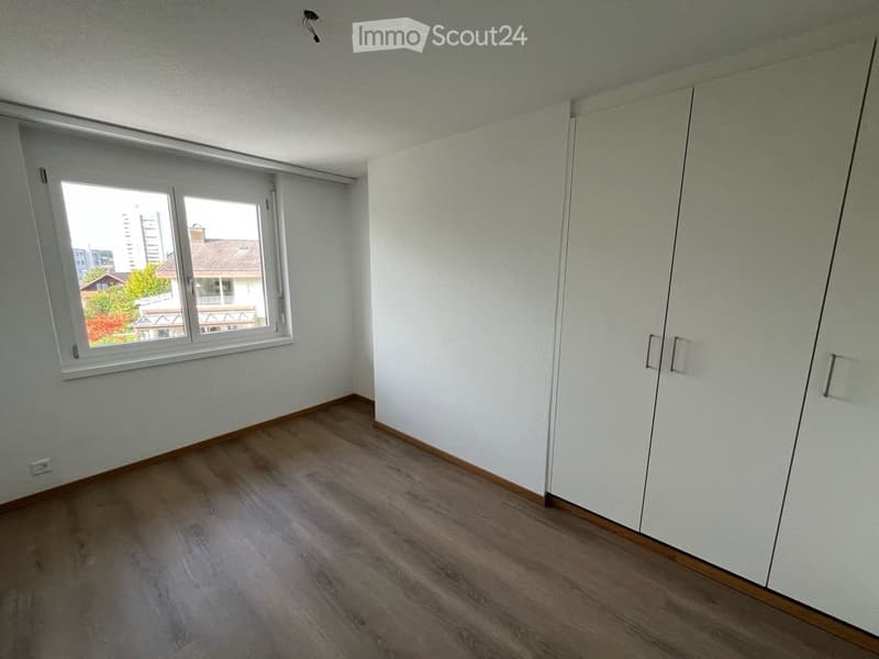 Empty room with wooden flooring, white walls, large window with view, and built-in closet.