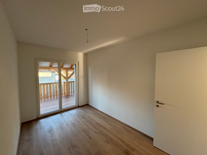 Empty room with light wooden flooring, white walls, and a sliding glass door leading to a wooden deck and outdoor area.