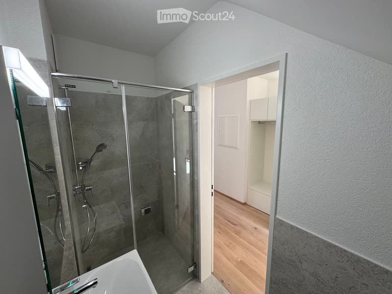 Modern bathroom with a bathtub, glass-enclosed shower, and wooden flooring.