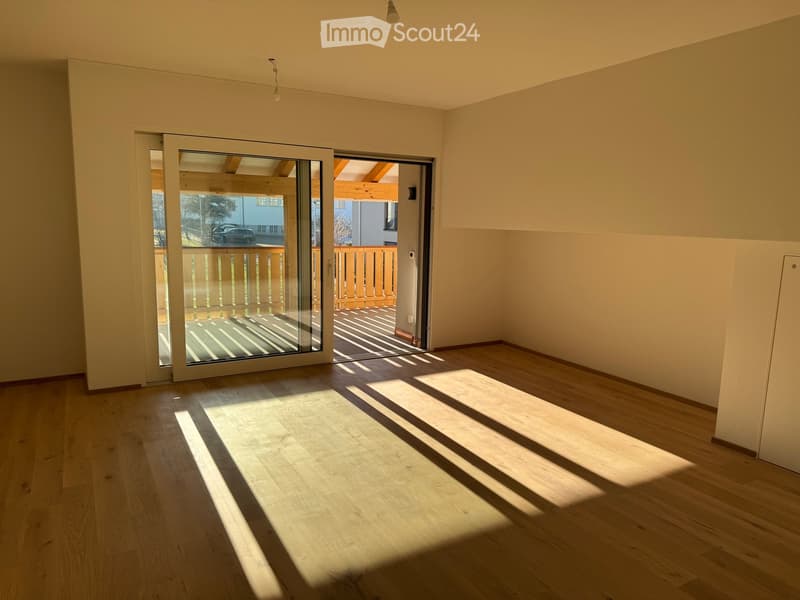 Empty room with wooden flooring, large sliding glass doors leading to a balcony, and natural light streaming in.