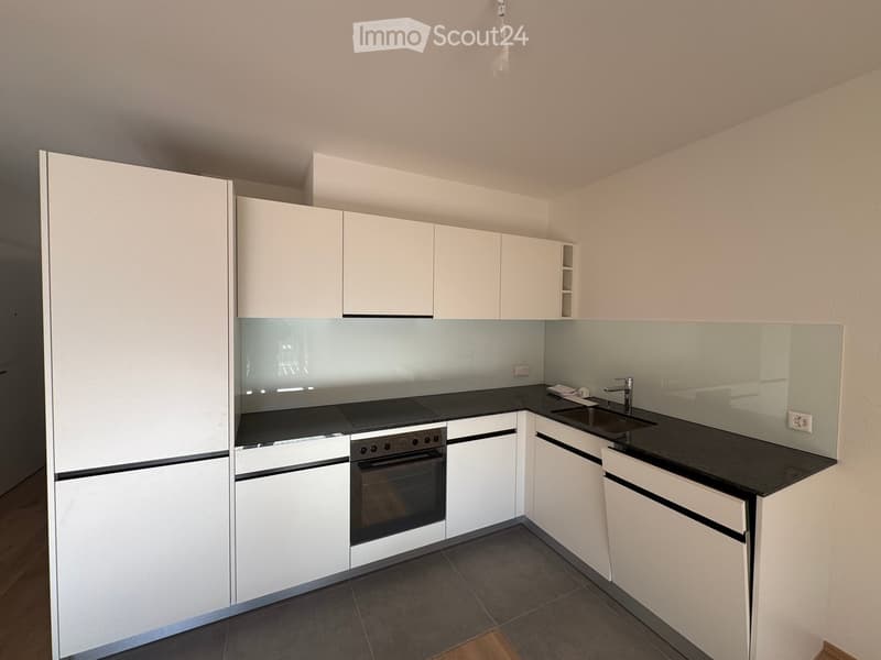 Modern kitchen with white cabinets, black countertops, and stainless steel appliances including an oven and sink.
